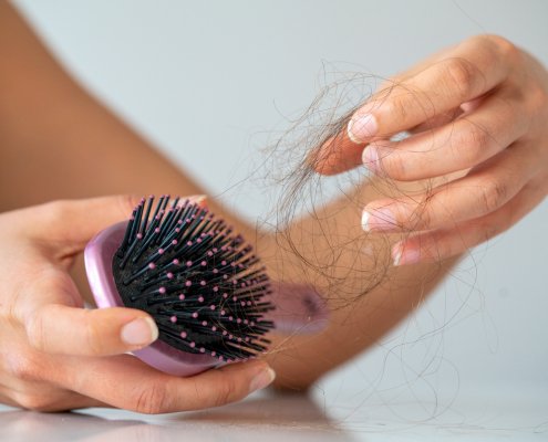 A woman holding a light pink hair brush and picking her hair out of it.