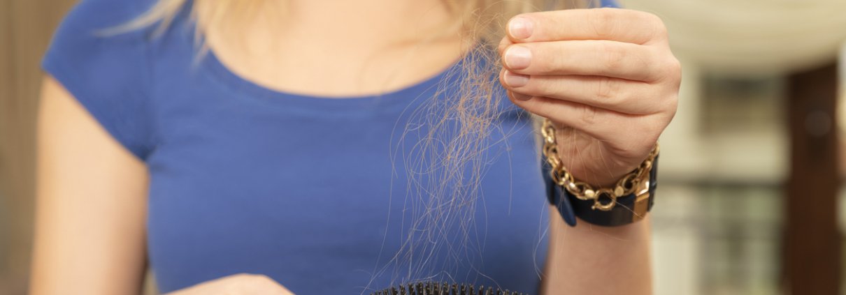 A woman brushing out her hair while she notices how thin it is and that it's falling out.