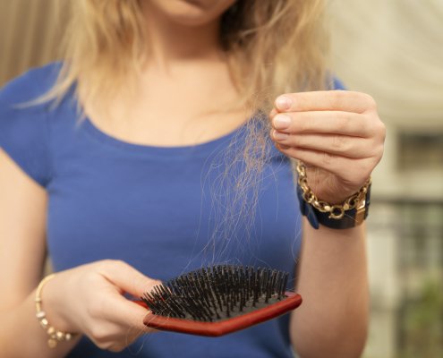 A woman brushing out her hair while she notices how thin it is and that it's falling out.