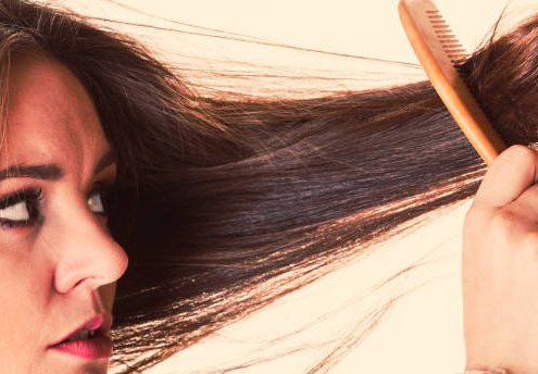 Dissatisfied woman combing with brush and pulls at her long hair. Feeling pain for nice look in daily activity.